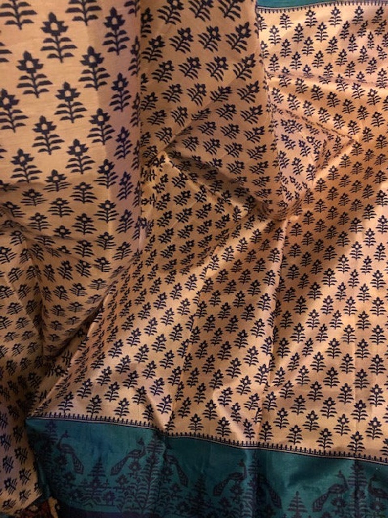 May include: A close-up of a fabric with a repeating pattern of black floral designs on a light brown background. The fabric has a green border with a black floral design.