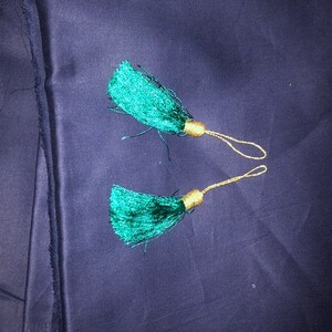 May include: Two green tassel ornaments with gold cords. The tassels are on a dark blue fabric background.