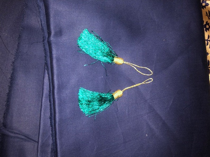 May include: Two green tassel ornaments with gold cords. The tassels are on a dark blue fabric background.