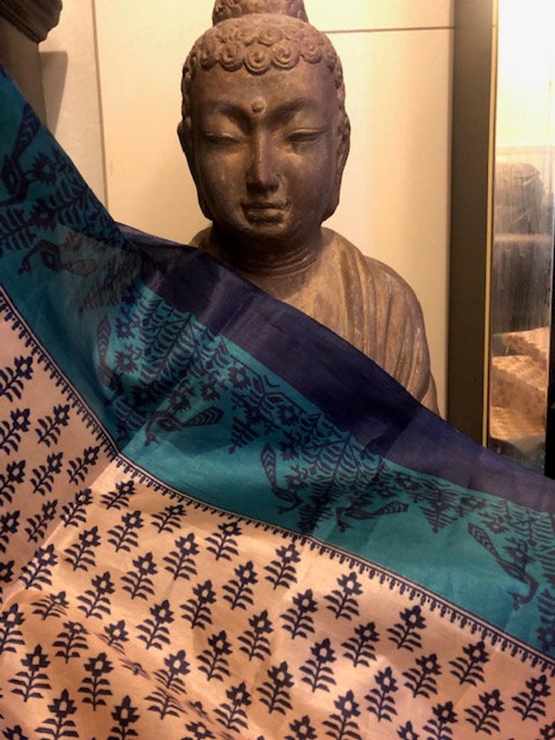 May include: A blue and teal patterned silk scarf draped over a brown statue of Buddha. The scarf has a cream background with a black floral design.