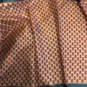 May include: A beige fabric with a repeating pattern of small black floral designs. The fabric has a green border with a black floral design.