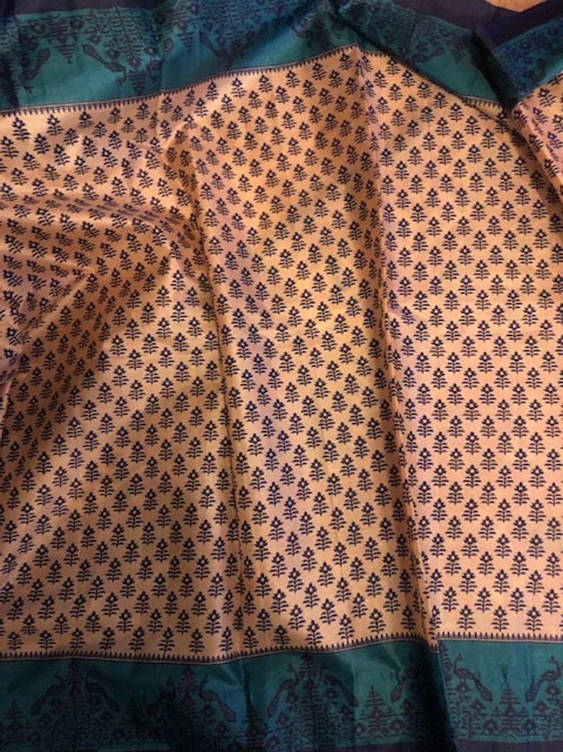 May include: A beige fabric with a repeating pattern of small black floral designs. The fabric has a green border with a black floral design.