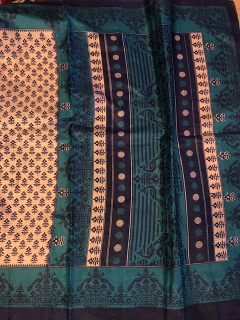 May include: A blue and white patterned fabric with a repeating design of peacocks and floral motifs. The fabric has a textured surface and a subtle sheen.
