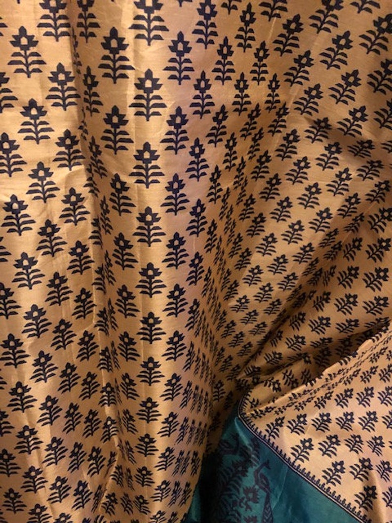 May include: A close-up of a fabric with a repeating pattern of black floral designs on a gold background. The fabric is folded in half, revealing a green fabric with a similar pattern on the bottom.