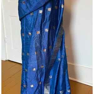 May include: A blue silk saree with a gold floral pattern. The saree is draped over a mannequin and has a silver border.