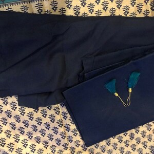 May include: Two pieces of dark blue fabric with teal tassels. The fabric is folded and laid on a patterned surface.