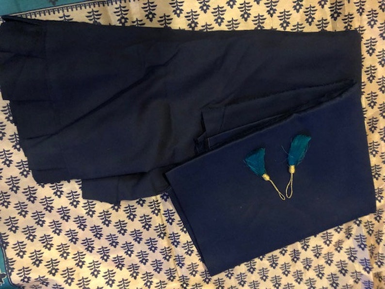 May include: Two pieces of dark blue fabric with teal tassels. The fabric is folded and laid on a patterned surface.