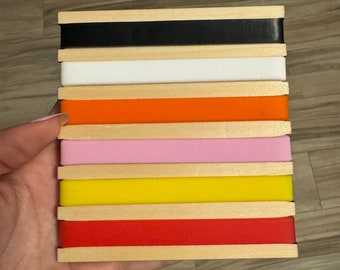 Op de afbeelding: Een stapel van acht houten blokken met verschillende gekleurde elastiekjes. De kleuren zijn zwart, wit, oranje, roze, geel, rood en nog twee tinten rood.