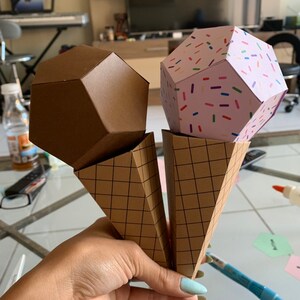 Puede incluir: Dos conos de helado de papel con bolas de helado geom&eacute;tricas. Las bolas de helado son marrones y rosas con chispas de colores. Los conos son marrones con un patr&oacute;n de cuadr&iacute;cula.