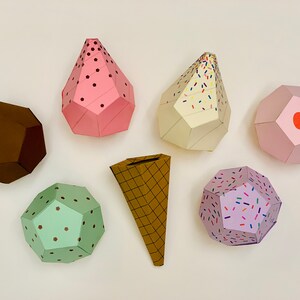Puede incluir: Un conjunto de seis conos y bolas de helado de papel. Los conos son marrones con un patr&oacute;n de gofres. Las bolas son rosas, verdes, moradas y blancas con diferentes chispas y dise&ntilde;os.