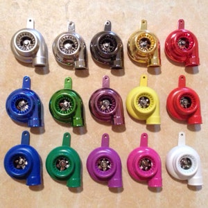 Puede incluir: Una colección de 15 réplicas de turbocompresores en miniatura en varios colores, incluyendo plata, negro, oro, rojo, morado, amarillo, azul, verde, rosa y blanco. Cada réplica presenta un diseño detallado con un impulsor plateado.