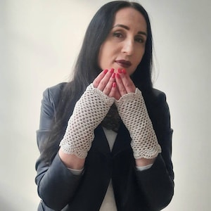 May include: A woman wearing a black leather jacket with a white crocheted fingerless glove on each hand. The gloves have a scalloped edge.