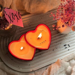 May include: Two red heart-shaped candles with the words "I LOVE YOU" on one candle. The candles are lit and glowing.