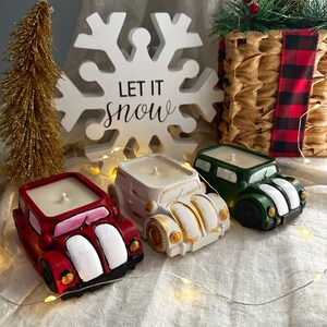 May include: Three vintage car shaped candles, one red, one white, and one green, with the text "Let it Snow" on a white snowflake cutout behind them.
