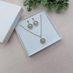 May include: A silver necklace and earrings set with a dandelion design. The necklace and earrings are in a white box.