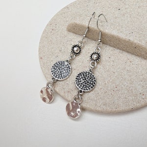 May include: Silver dangle earrings with two round textured discs and a smaller hammered disc at the bottom of each earring.
