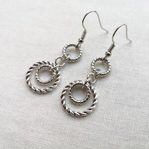 May include: Silver dangle earrings with two intertwined circles. The circles are connected by a small chain.