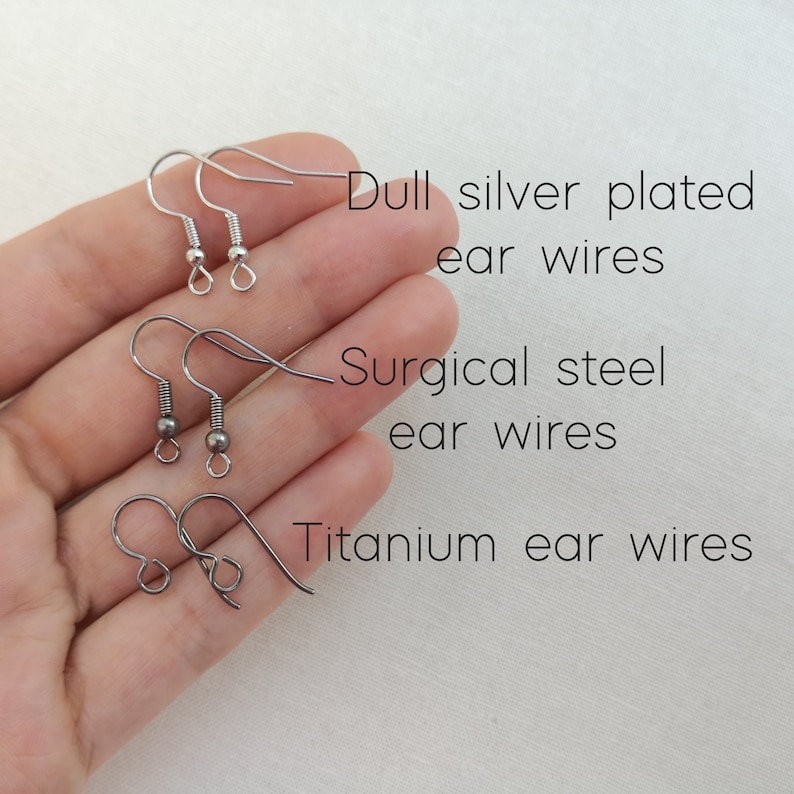 Ear wire option are presented on a hand. The options are either dull silver plated, surgical steel ear wires or titanium ear wires.