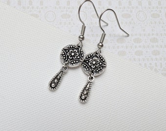 May include: Silver dangle earrings with a floral design. The earrings have a round, filigree charm with a smaller flower in the center. The charms are attached to a teardrop-shaped dangle with small beads.