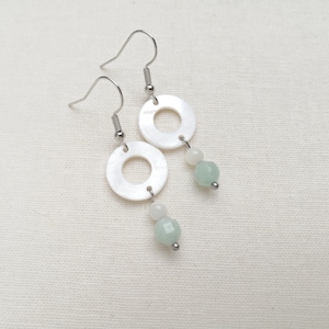 May include: A pair of silver hoop earrings with white shell and light green gemstone accents.