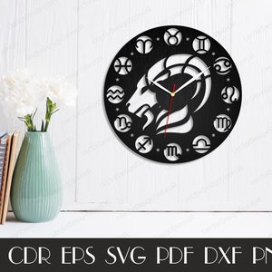 May include: Black and white clock face with a zodiac design. The clock face features a ram's head in the centre, surrounded by the twelve zodiac signs. The clock hands are white and red.