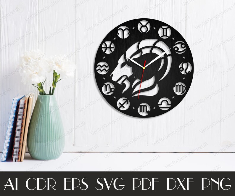 May include: Black and white clock face with a zodiac design. The clock face features a ram's head in the centre, surrounded by the twelve zodiac signs. The clock hands are white and red.