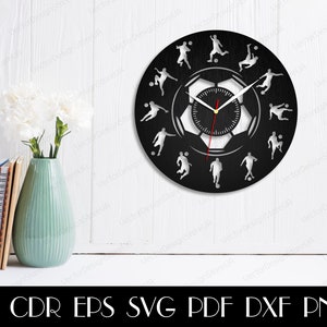 May include: Black and white clock with a soccer ball design. The clock face features a soccer ball with a clock face inside. The clock hands are red. The clock is surrounded by 12 soccer players in various poses.