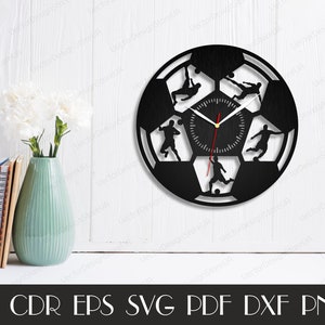 May include: Black and white silhouette of a soccer ball with five soccer players in action. The clock face is in the center of the ball. The clock hands are red and gold.