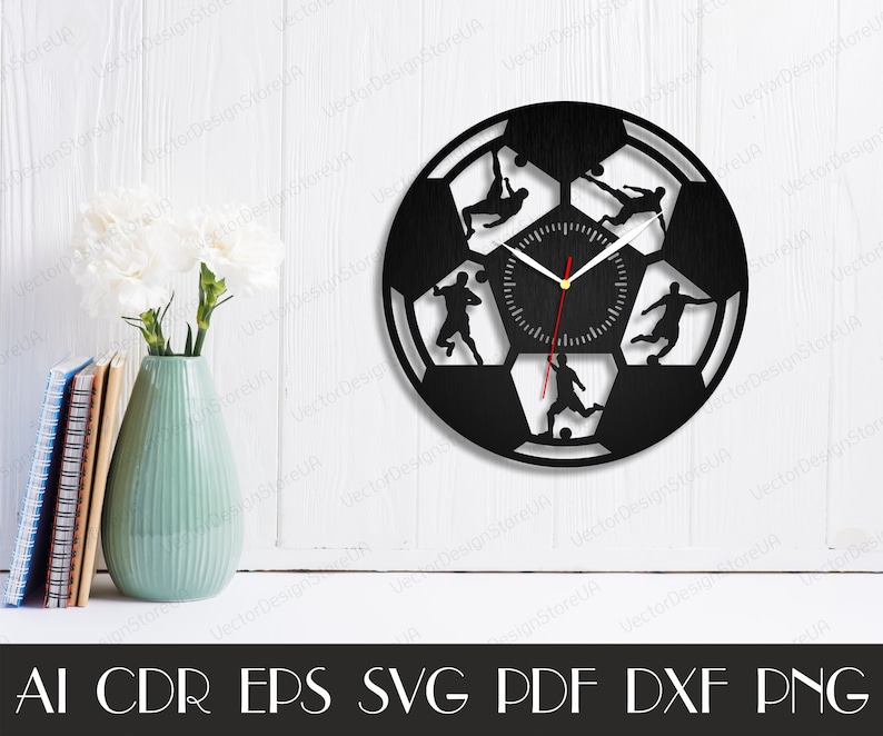 May include: Black and white silhouette of a soccer ball with five soccer players in action. The clock face is in the center of the ball. The clock hands are red and gold.
