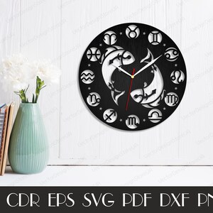 May include: Black and white clock with a circular design featuring the astrological signs of the zodiac. The clock face is made of wood and has a black background. The clock hands are red and white. The clock is surrounded by a white border.