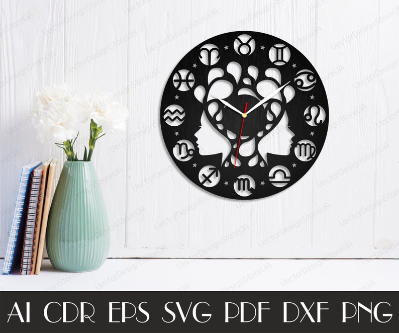 May include: Black wall clock featuring zodiac symbols around the perimeter. The clock face has two profile silhouettes and a decorative design. The clock hands are red. The clock is displayed on a white surface. The image also includes a vase with flowers and books.