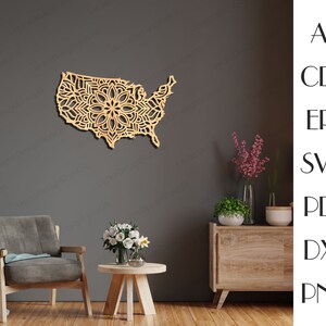 May include: A wooden wall decor in the shape of the United States with a mandala design. The decor is hanging on a gray wall above a wooden table and a brown armchair.