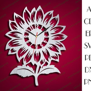 May include: A silver metal clock in the shape of a sunflower with a white face and black hands. The clock face has black numbers and a gold center. The sunflower has a detailed design with petals and leaves.