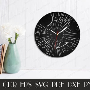 May include: A black wooden clock with a white space-themed design. The clock face features a stylized sun with rays, planets, and stars. The clock hands are red and silver. The clock face also includes the word "Space".