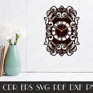 May include: A decorative wooden wall clock with an ornate, scrollwork design. The clock face is dark brown with gold hands and a red second hand. The clock is rectangular with a detailed border. The image also shows a vase with flowers and books.