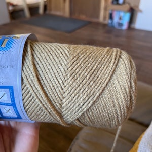 K&ouml;nnte beinhalten: Eine Garnrolle in beige mit einem blauen und wei&szlig;en Etikett. Das Etikett enth&auml;lt den Text "HL # 519" und "GAUGE 18sts (10 X 10 cm)".