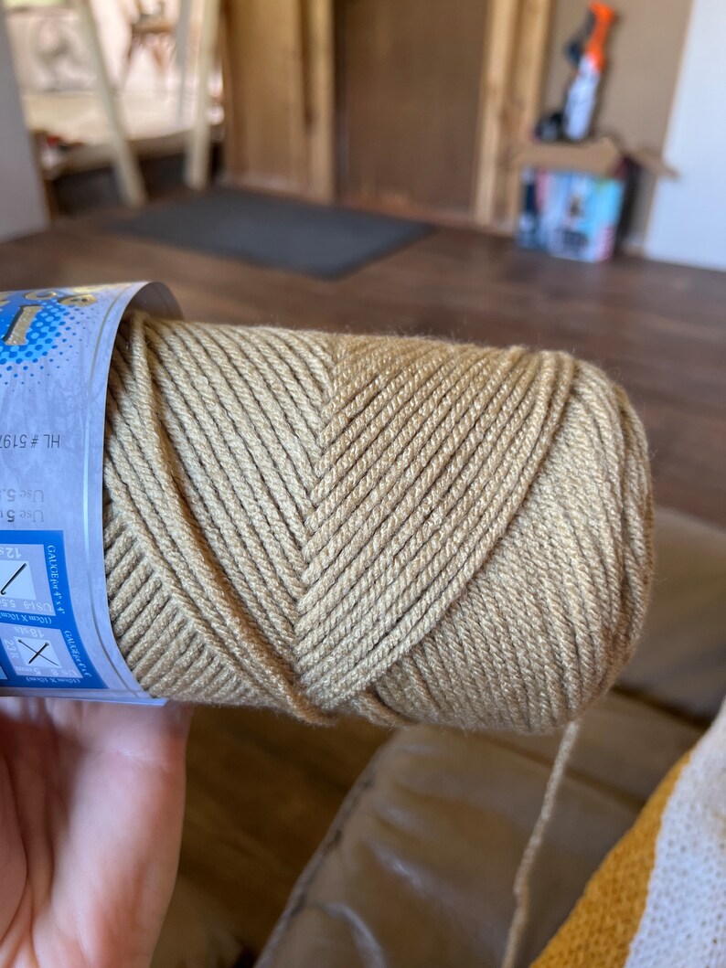 K&ouml;nnte beinhalten: Eine Garnrolle in beige mit einem blauen und wei&szlig;en Etikett. Das Etikett enth&auml;lt den Text "HL # 519" und "GAUGE 18sts (10 X 10 cm)".