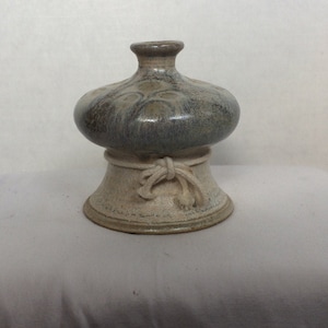 Puede incluir: Un jarrón de cerámica con una parte superior bulbosa y una base de pedestal. La parte superior es de un gris-azul moteado, mientras que la base es de un beige moteado. Un diseño decorativo en forma de cuerda adorna la base. El jarrón es un artículo decorativo único.