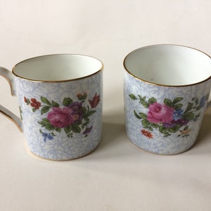 Puede incluir: Dos tazas de café de porcelana con un diseño floral. Las tazas tienen un fondo azul claro con un patrón delicado y presentan una rosa rosa y otras flores coloridas. Los bordes y las asas están adornados con oro.