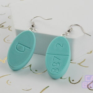 May include: A pair of turquoise pill-shaped earrings with silver hooks. One earring has the number "2" on one side and "887" on the other. The other earring has the letter "D" on it.