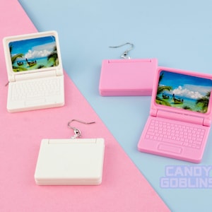 Könnte beinhalten: Ein Paar Laptop-Ohrringe. Ein Ohrring ist pink und hat einen Bildschirm mit einer Strandszene. Der andere Ohrring ist weiß und hat einen leeren Bildschirm. Beide Ohrringe haben einen silbernen Haken.