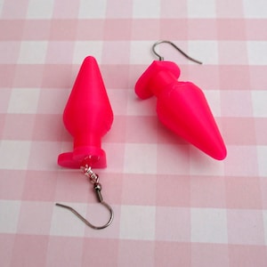 May include: A pair of pink, cone-shaped earrings with silver hooks. The earrings are made of a smooth, rubber-like material.