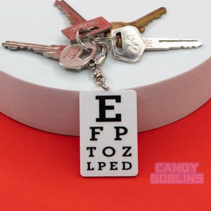 May include: White eye chart keychain with black letters spelling "E F P T O Z L P E D". The keychain is attached to a set of keys.