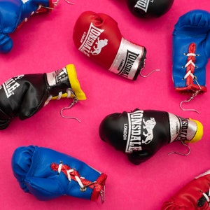 May include: Assortment of boxing glove earrings in various colours, including red, blue, black, and yellow. Each earring features the Lonsdale London logo and a lion graphic.