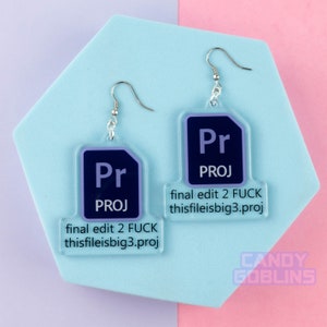 Könnte beinhalten: Ein Paar silberne Ohrringe mit transparenten Acryl-Anhängern, die das Adobe Premiere Pro-Logo und den Text "final edit 2 FUCK thisfileisbig3.proj" zeigen.