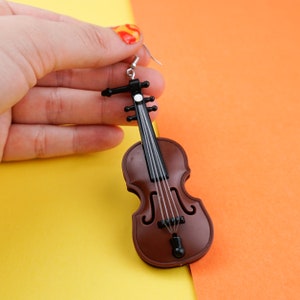 May include: A brown violin-shaped earring with black details and a silver hook. The earring is made of plastic and is a fun and whimsical accessory.