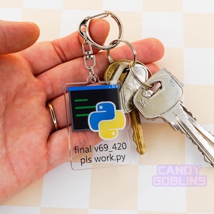 A hand holds our Python keychain that is attached to a set of keys. The keychain features the Python logo, with text underneath that reads "final v69_420 pls work.py".