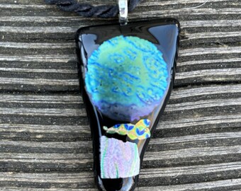 May include: A black glass pendant necklace with a blue and green abstract design. The pendant is shaped like a teardrop and has a silver bail.
