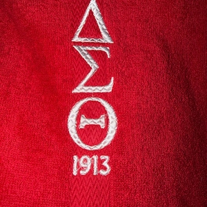 May include: Close-up of a red towel with white embroidered Greek letters and the number 1913. The Greek letters are arranged vertically, with a triangle at the top, followed by a sigma, a zeta, and a circle with a horizontal line through it.
