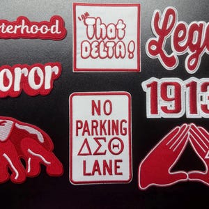 Peut inclure: Un ensemble d'écussons brodés rouges et blancs avec les textes Sisterhood, Soror, I AM THAT DELTA!, Legacy, 1913 et NO PARKING DELTA LANE. Le lot comprend un motif d'éléphant et un symbole de geste de la main avec des lettres grecques.